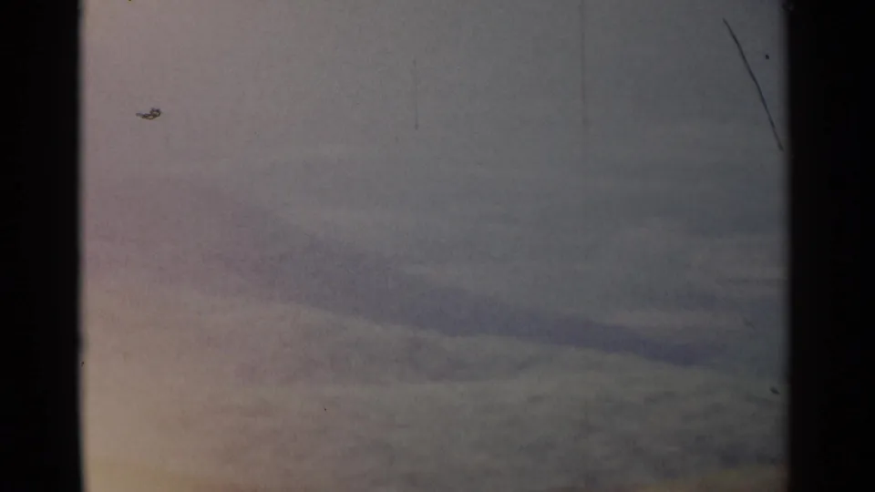 1962 8mm frame showing a distant ridgeline beneath a gray-blue sky, partially obscured by a dark film edge.
