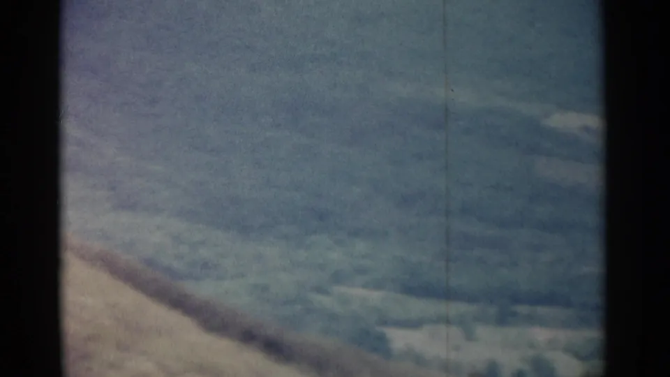 1962 8mm frame of hazy slopes and distant terrain, with pale sky and visible film wear along the edges.