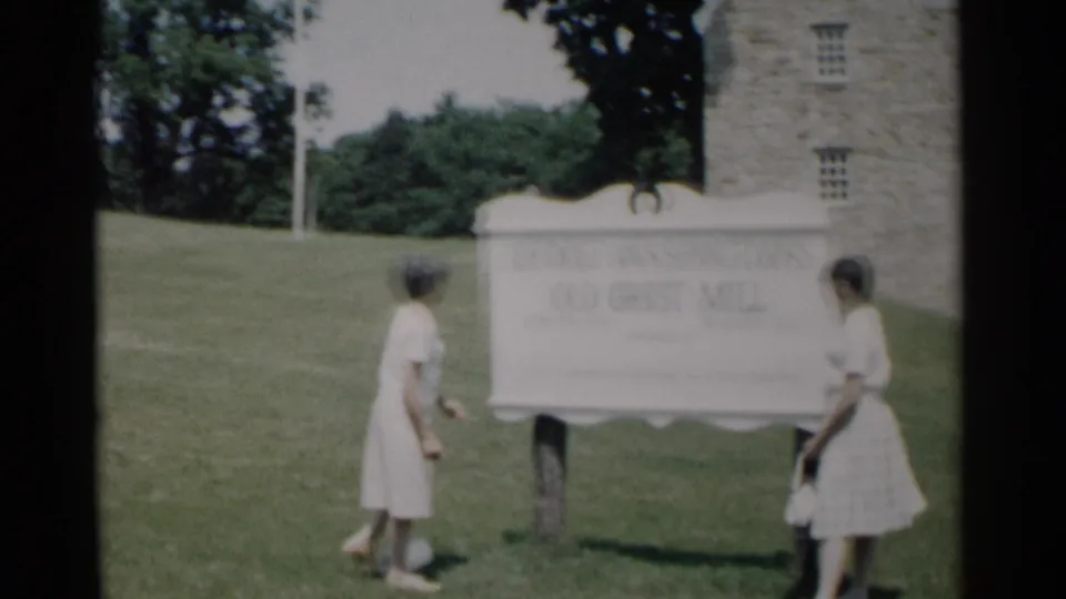 Two young women pause around the George Washington's Old Grist Mill sign during a 1962 Jamestown visitor stop.