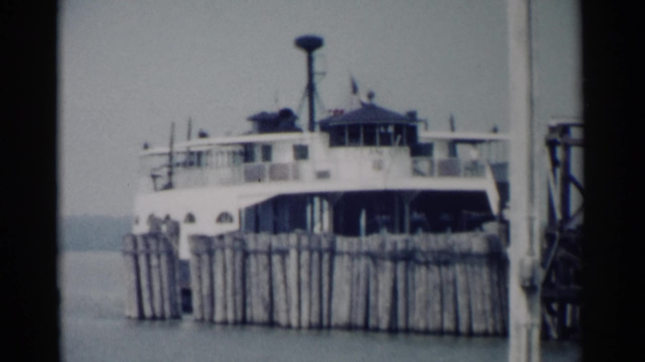 White ferry docked beside wooden pilings with water in the background.