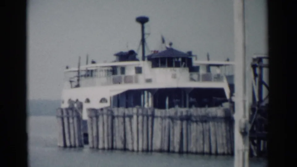 1962 Jamestown, Virginia home-movie frame showing a white ferry moored beside a wooden pier and pilings.
