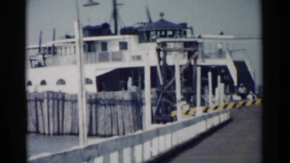 1962 Jamestown, Virginia frame showing the ferry, dock railing, ramp structure, and distant people near the waterfront.