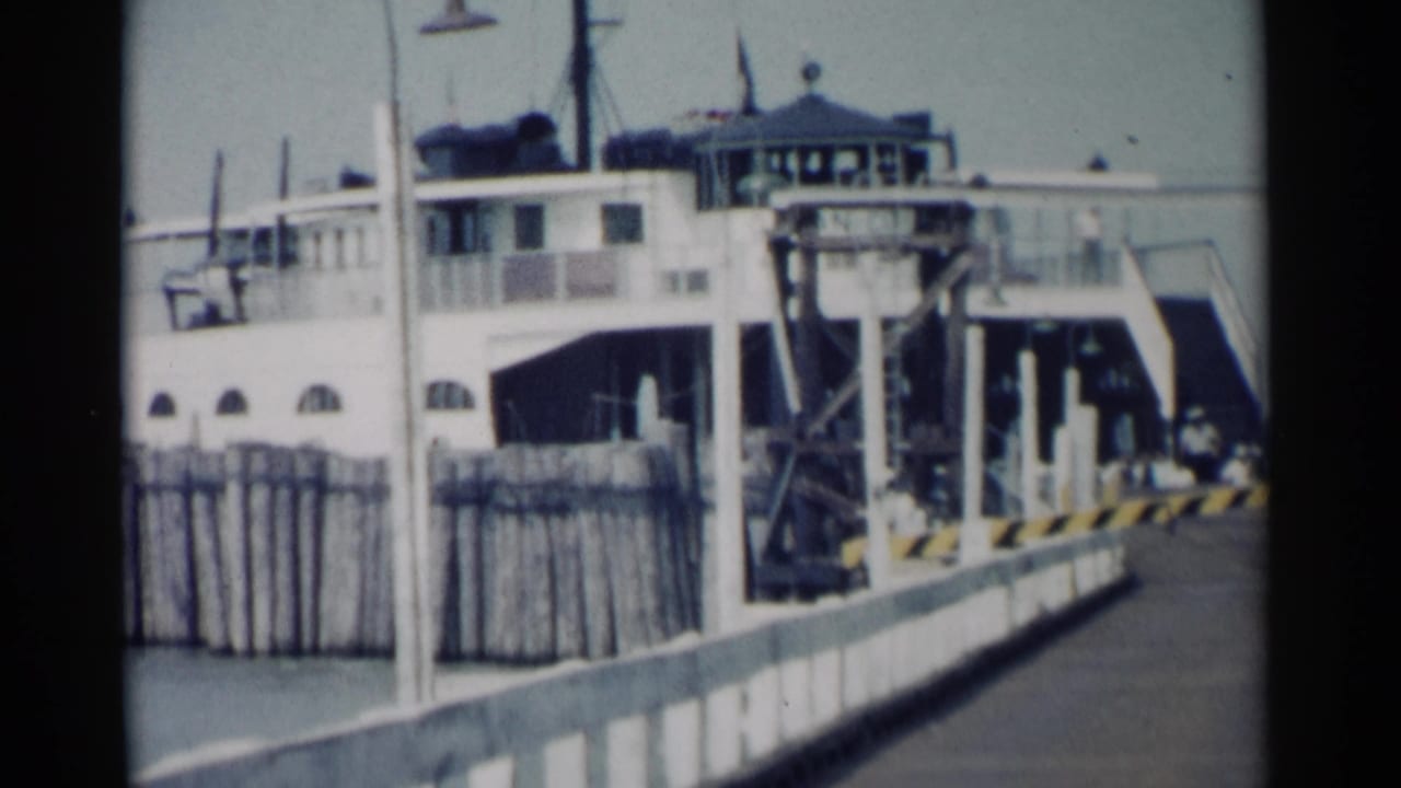 White ferry docked beside a wooden pier with ramp structure and railings.