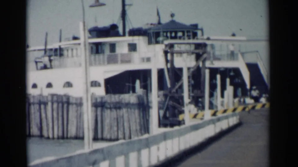 1962 Jamestown, Virginia ferry at a pier, with arched windows, a loading ramp, railings, and open water partly visible.