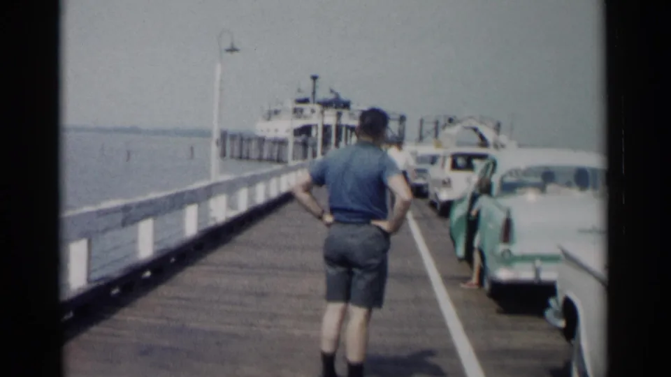 The Jamestown ferry landing appears from a visitor viewpoint, with a man on the pier and cars lined up beside the water.