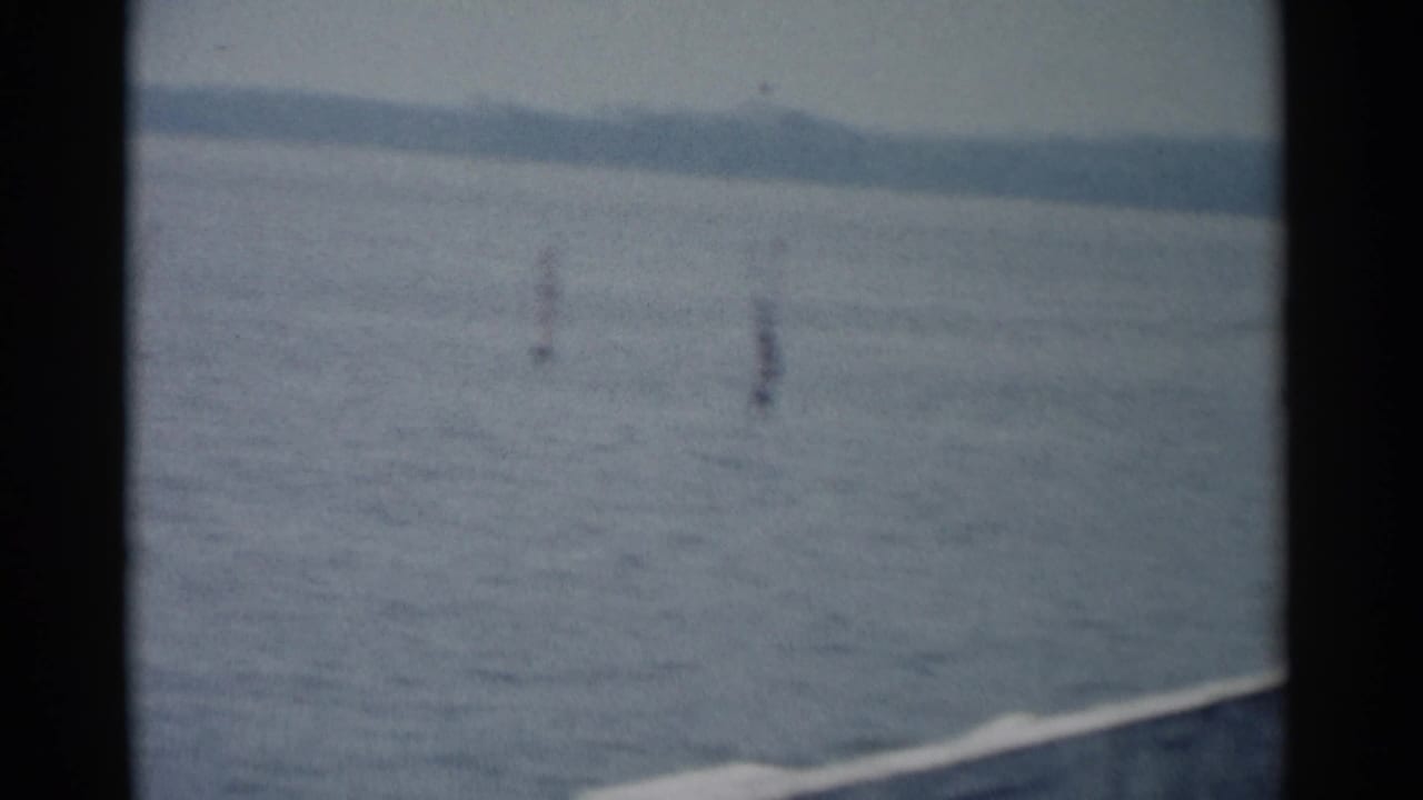 1962 Jamestown, Virginia home-movie frame showing calm river water, distant shoreline, and small water markers through soft 8mm framing.