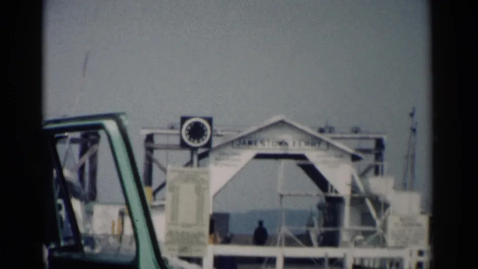 Jamestown, Virginia ferry dock in 1962 with white landing structure, ramp, railings, vehicle window, and small figures near the water.