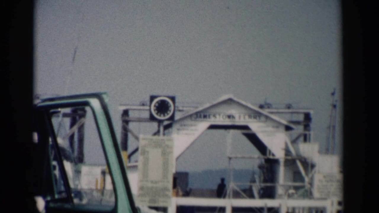 Jamestown Ferry sign and clock above a ferry landing, with a green vehicle partly visible in front.