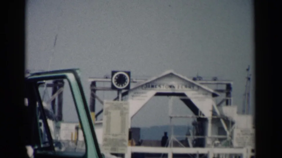 1962 Jamestown, Virginia ferry terminal view with the Jamestown Ferry sign, clock, dock structure, water, and a green vehicle edge.