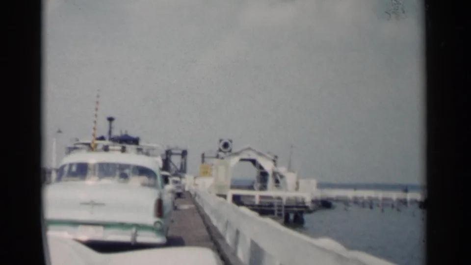 A white 1950s sedan approaches or waits near the ferry ramp at a Jamestown, Virginia waterfront dock in 1962 home-movie footage.