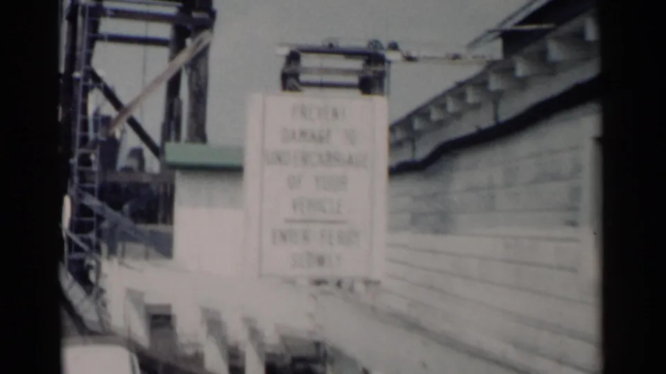 The ferry loading area in Jamestown, Virginia appears with a large warning sign, wooden approach railings, and metal machinery above the ramp.