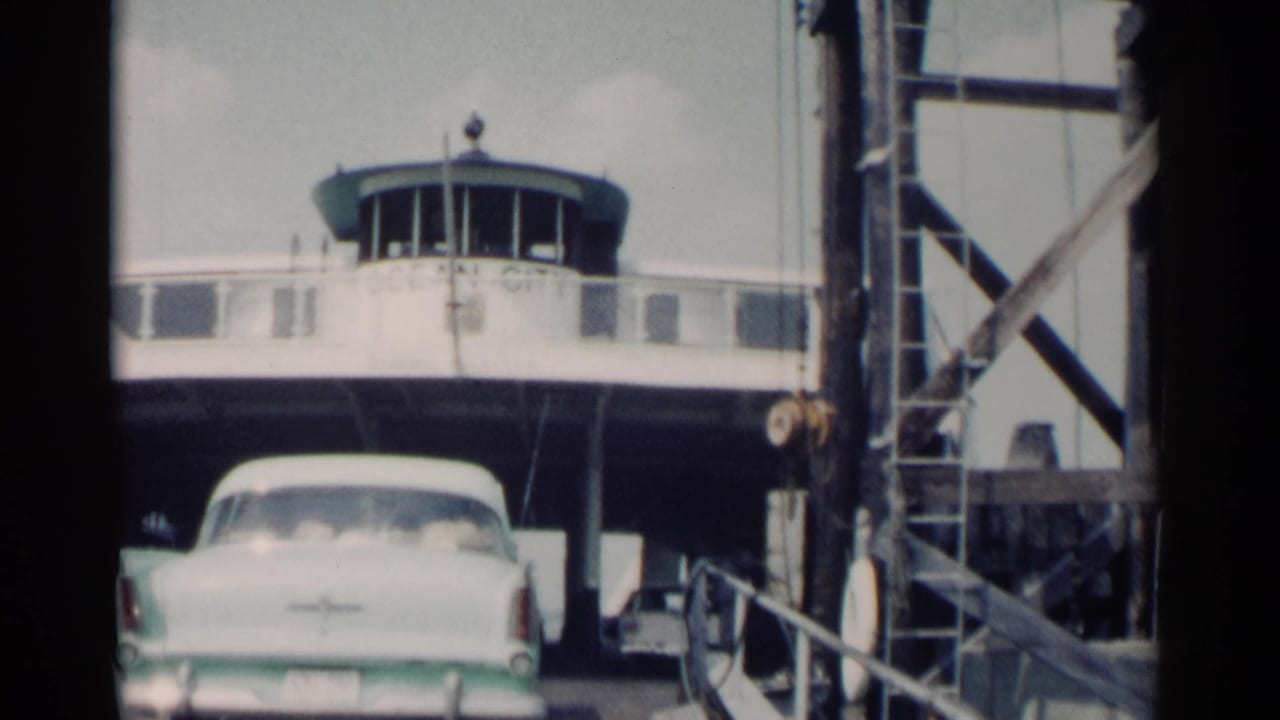 White classic car approaches a ferry ramp beneath a white pilot house.