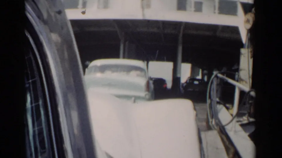 Close home-movie view of a white classic car near the ferry railings during boarding in the Jamestown travel sequence.