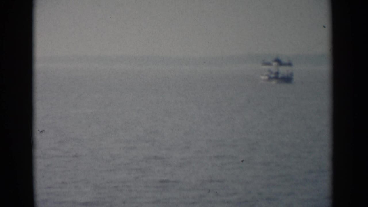 Distant small boat on calm water under a hazy sky, framed by dark film edges.