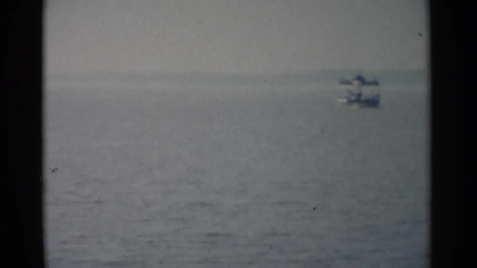 1962 Jamestown, Virginia 8mm frame showing a distant small boat on gray-blue water beneath a hazy sky.