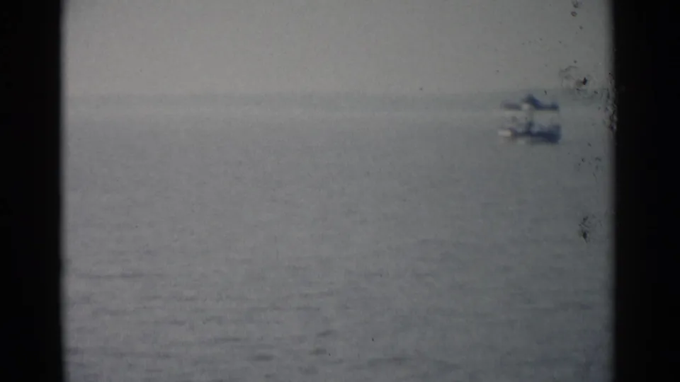 1962 Jamestown, Virginia 8mm frame showing a blurred distant boat on calm water with visible film wear.
