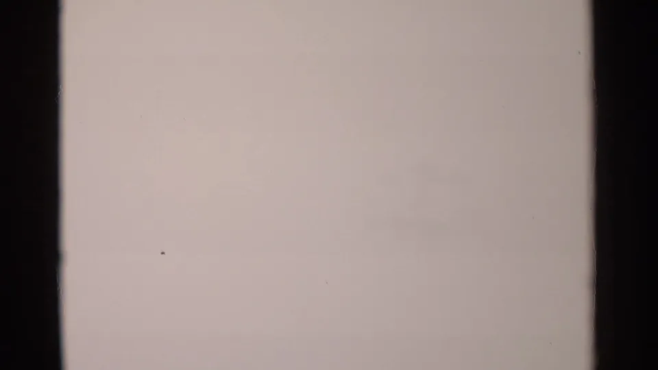 Overexposed 1962 8mm frame from the Jamestown clip, with only pale tone, film borders, and a small speck visible.