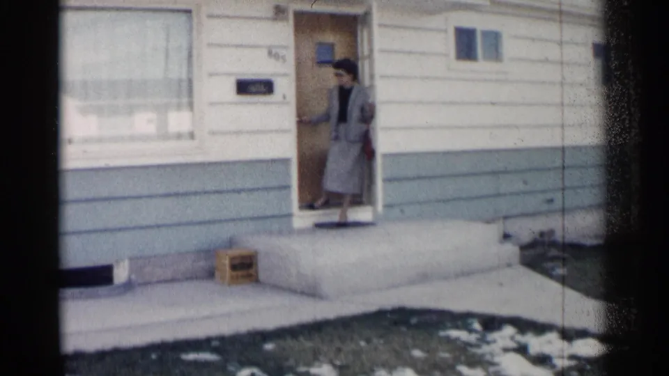 In Washington, DC 1962 home-movie footage, a woman in a gray suit and sunglasses steps out through a front door.