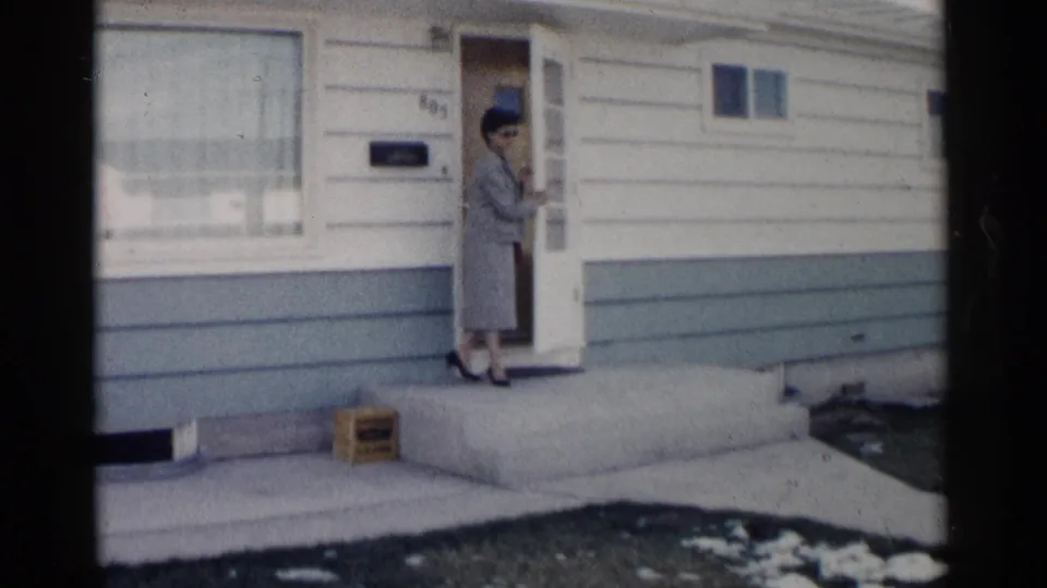 The woman pauses beside the open front door of a Washington, DC residence, with a mailbox and winter ground visible.