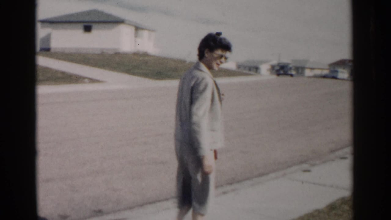 Woman in a grey suit walks on a suburban sidewalk beside a quiet street.