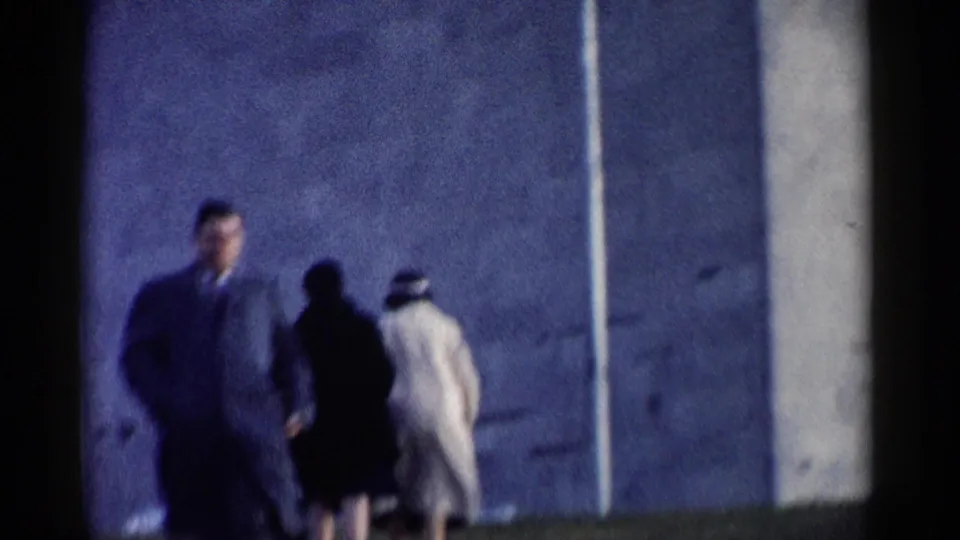 1962 Washington DC home-movie frame showing a suited man walking toward the camera, followed by two pedestrians near a landmark wall.