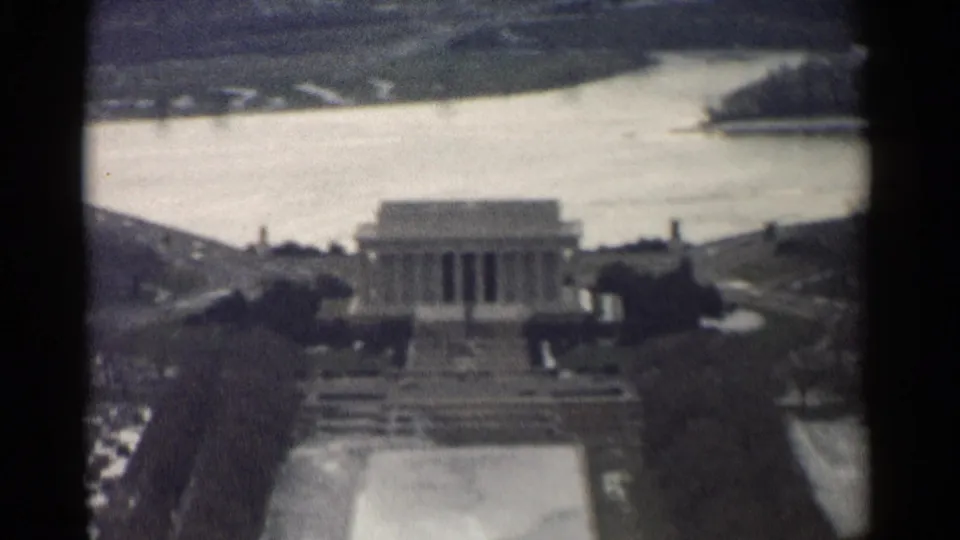 Soft 8mm aerial-style view of the Lincoln Memorial in Washington, DC, with water and a small wooded shoreline beyond.