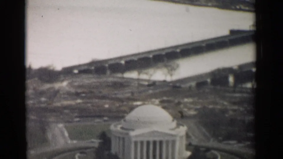1962 8mm view of the Jefferson Memorial in Washington, DC, framed from above with water, paths, trees, and a bridge in the distance.