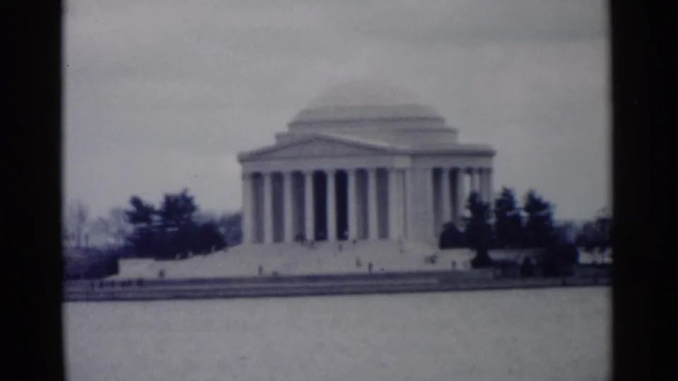 Washington, DC home-movie frame showing the Jefferson Memorial across the Tidal Basin with trees and small distant visitors near the steps.