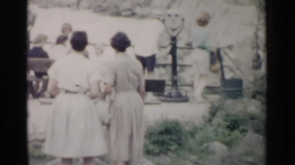 Two women stand beside scenic overlook viewfinders, with additional tourists faintly visible beyond them in Washington DC footage from 1962.