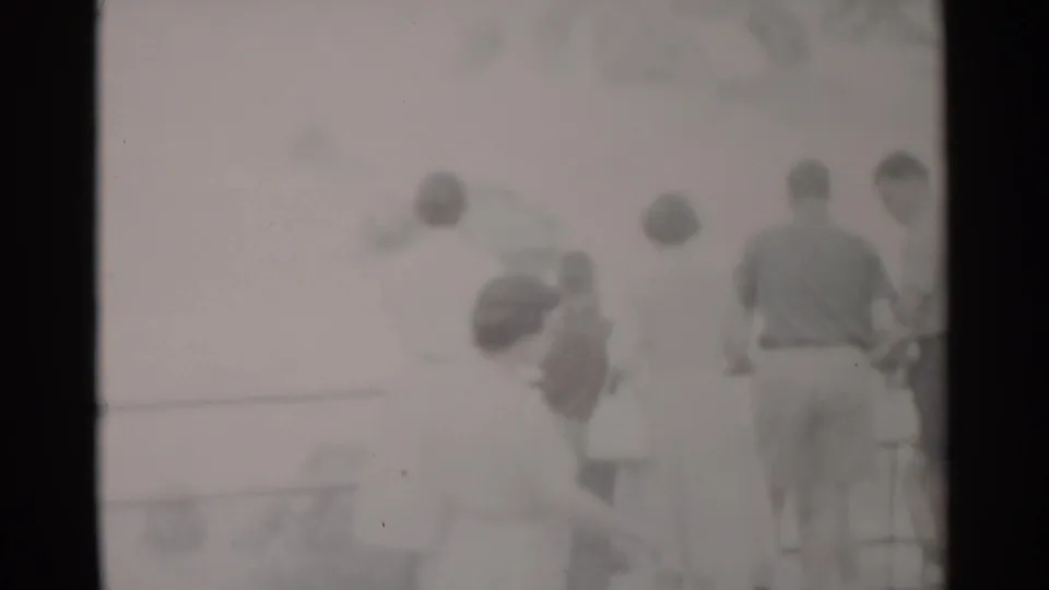 A small group of tourists stands at the overlook railing near a viewfinder, with the distant view washed out by bright 8mm exposure.
