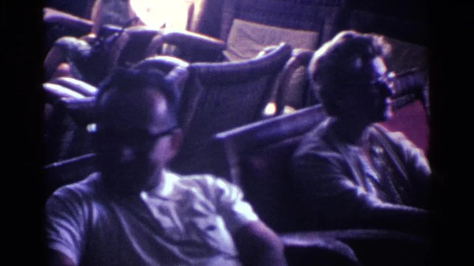 In the Kentucky living room scene, the man in glasses sits near the camera as another adult looks toward the side of the room.