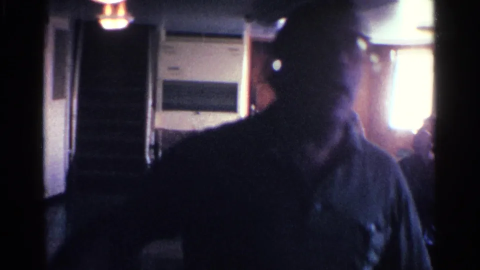1963 Kentucky home-movie frame with a silhouetted man in a dim interior, backlit by window and doorway light.