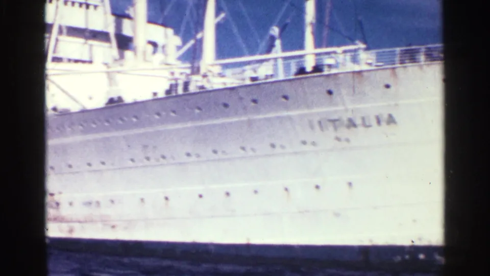 1963 8mm frame showing the white hull of the liner with ITALIA lettering, porthole rows, and upper deck railings.