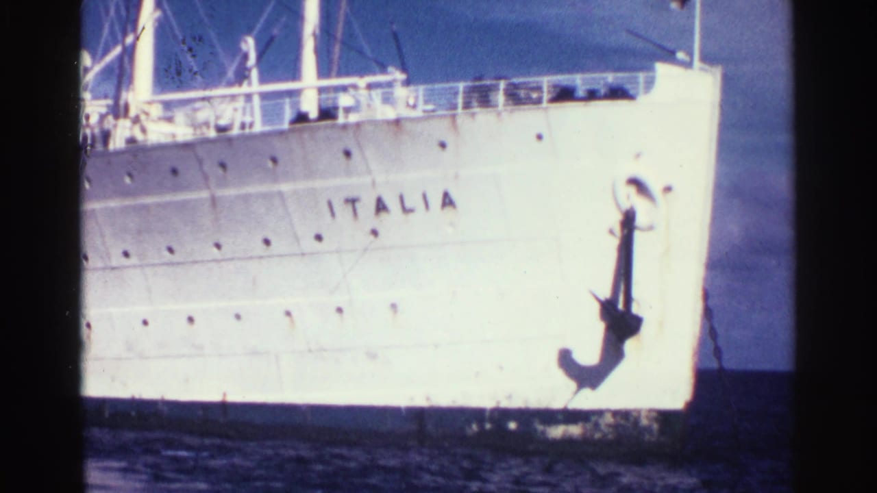 Close view of a white ship bow with ITALIA painted on the hull and a large anchor above blue water.