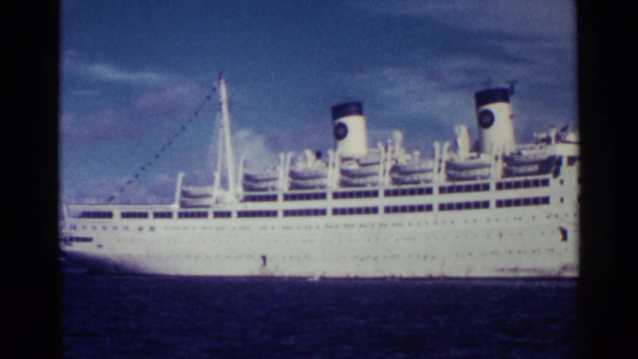 Large white ocean liner seen broadside on blue water beneath a cloudy sky.