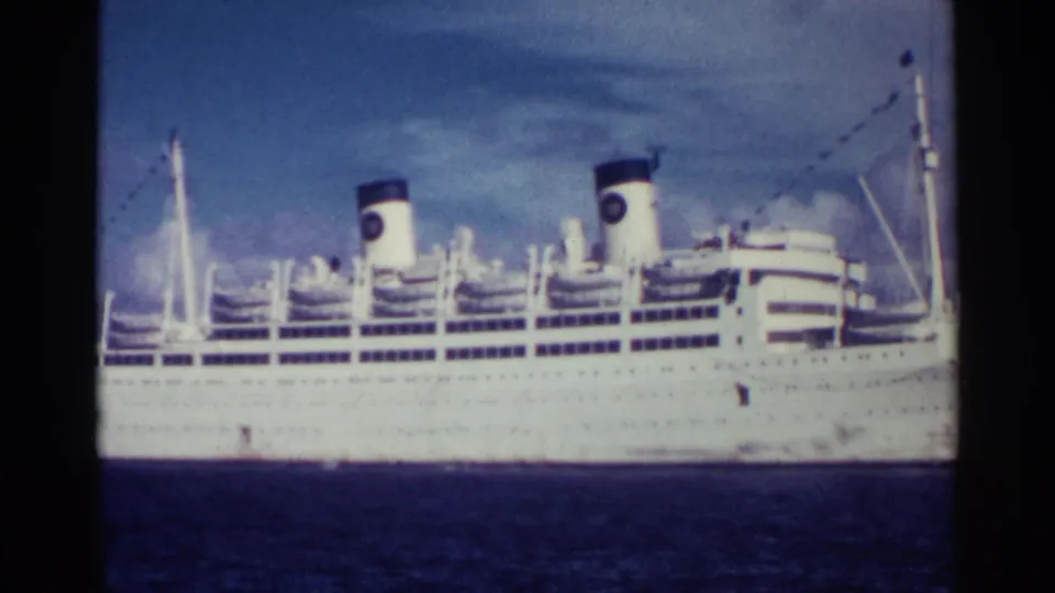 The liner remains in broadside view, showing two dark-capped funnels, upper decks, lifeboats, rigging, and deep blue water.