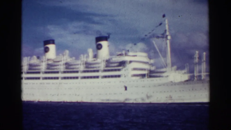 A cropped 8mm view centers on the liner's decks, funnels, lifeboats, rear rigging, white hull, and dark blue water.