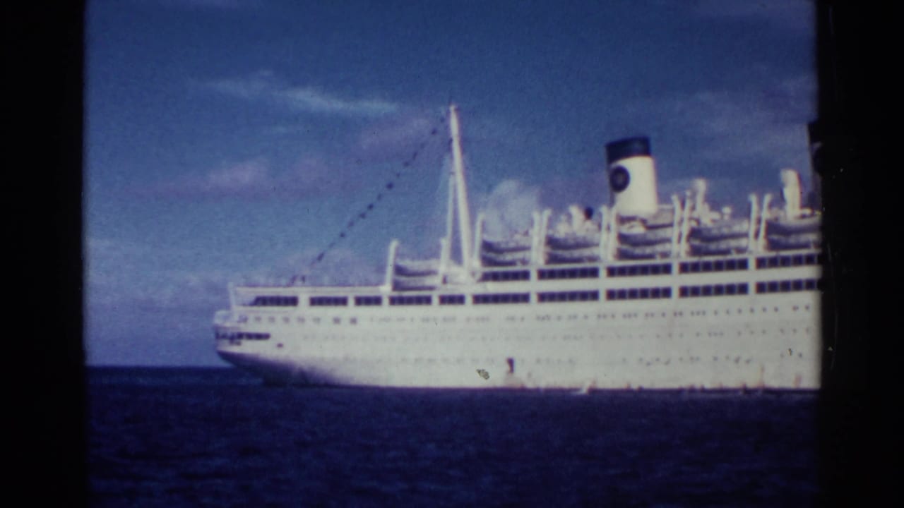 Large white ocean liner crossing blue water under a cloudy sky.