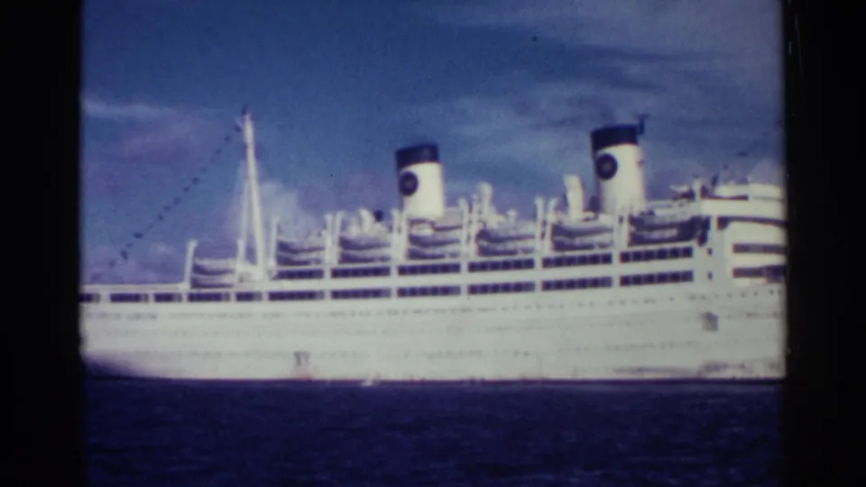 1963 Nassau frame showing the side of a large white liner with two dark-topped funnels and multiple passenger decks.