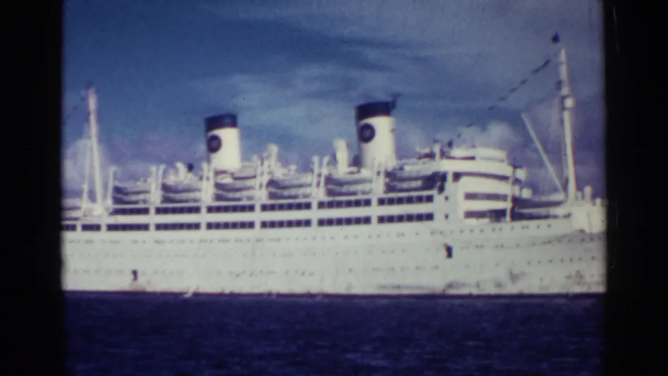1963 Nassau home-movie view of the liner's upper decks, lifeboats, two funnels, and mast rigging above the waterline.