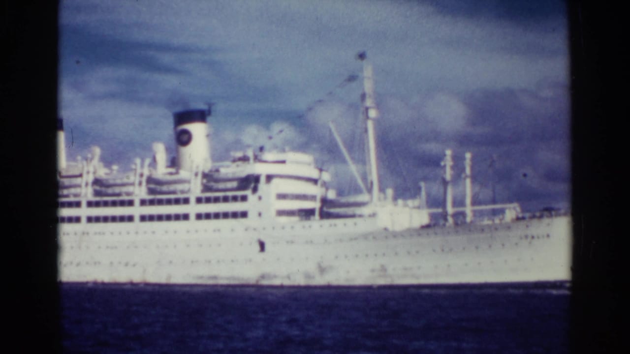 White passenger liner crossing dark-blue water beneath a cloudy sky.
