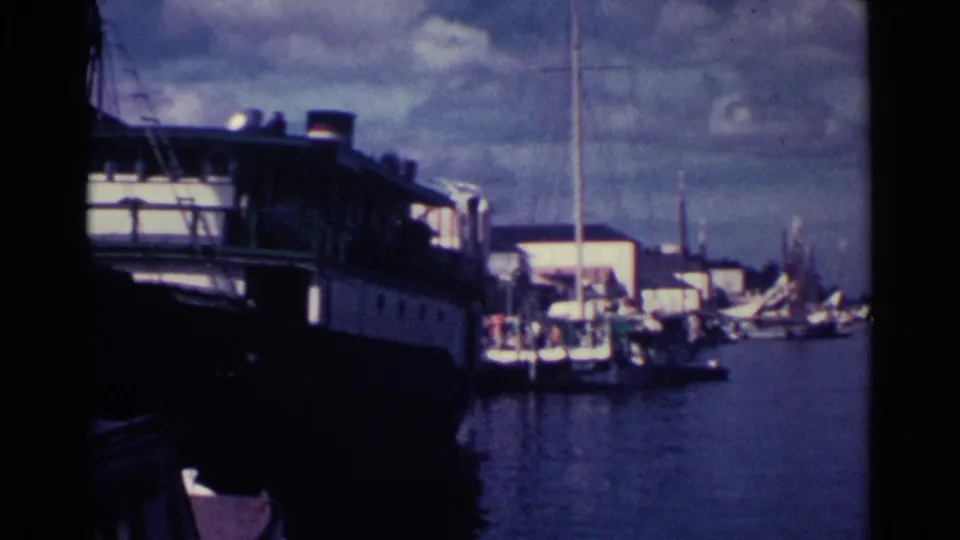 1963 Nassau dock scene with a large vessel at left, marina buildings, masts, and sailboats on calm harbor water.