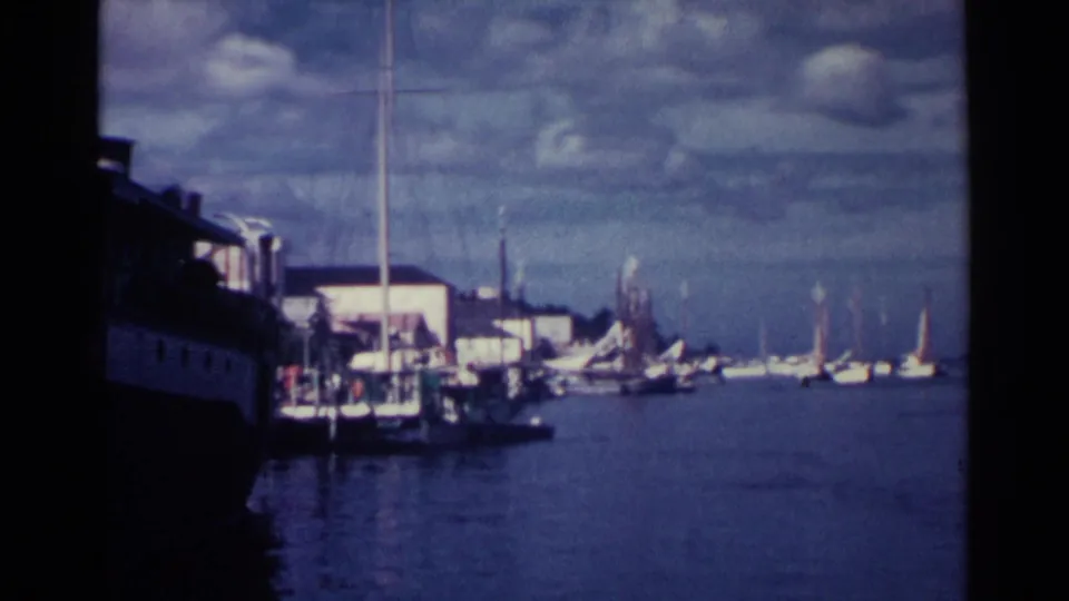 Nassau harbor in 1963, showing a docked vessel at left, sailboats at right, and low waterfront buildings under clouds.