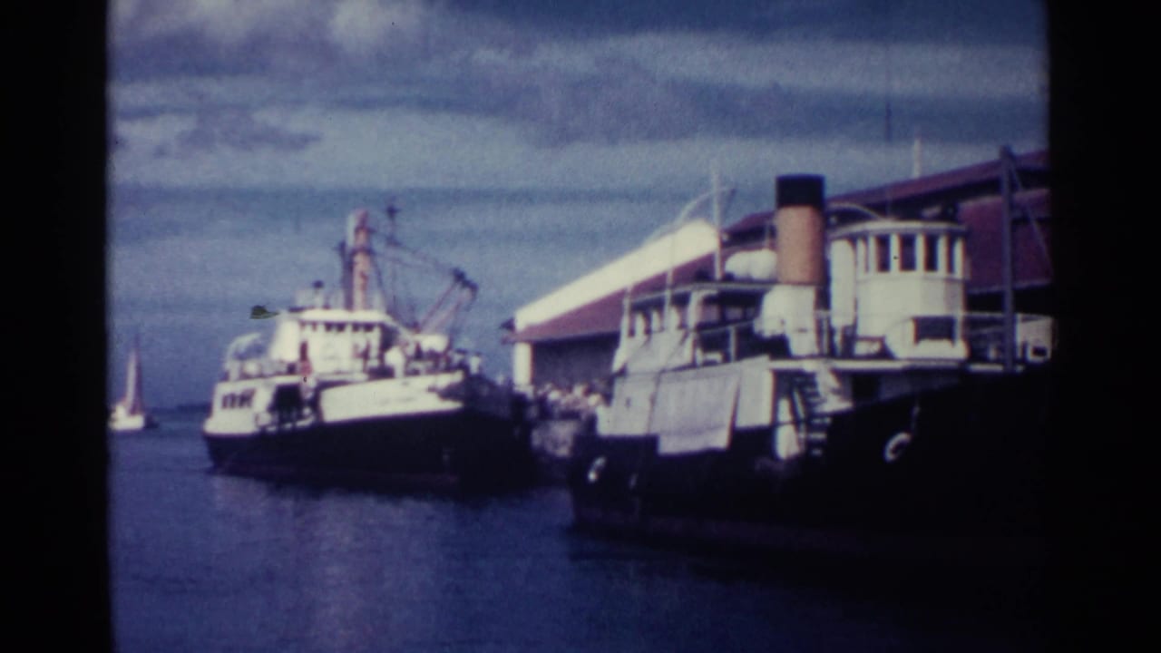 Docked boats beside a waterfront building under a cloudy sky.