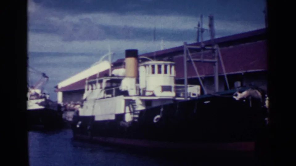 A dark-hulled vessel with a white superstructure is moored near a red-roofed dock building in Nassau, Bahamas.