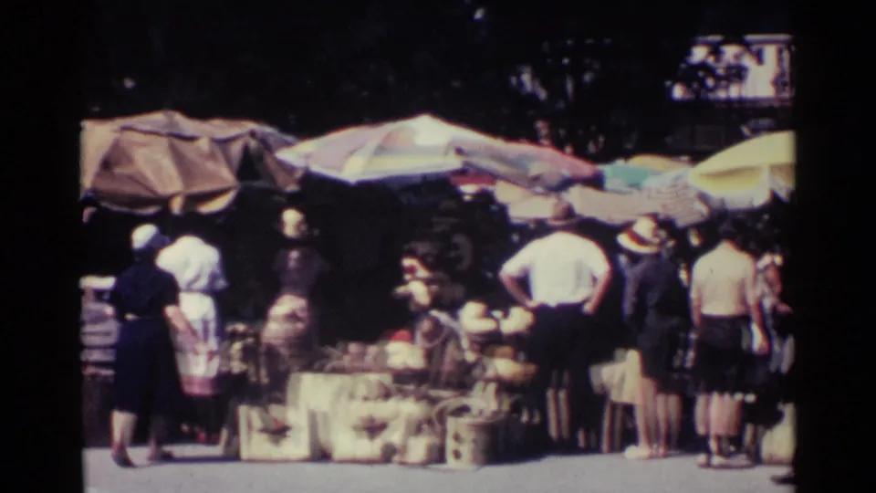 1963 Nassau street market scene with shoppers browsing under large umbrellas and goods displayed near the curb.