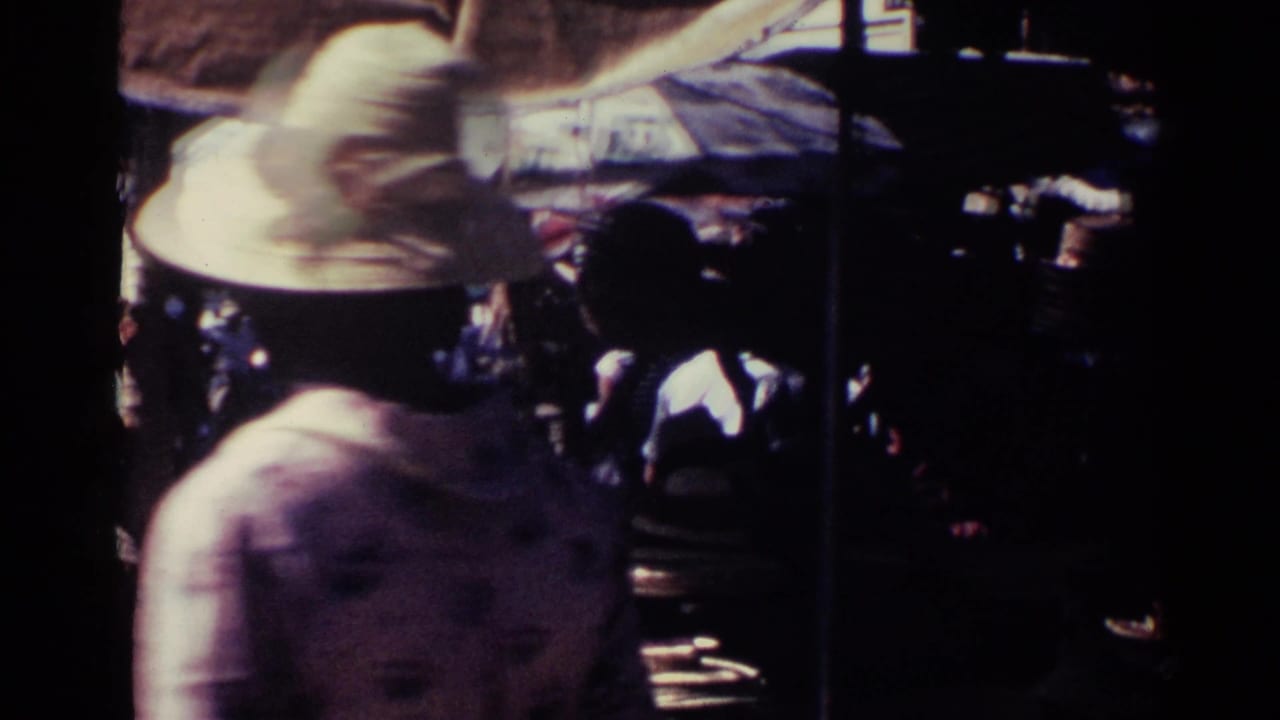 Partially obscured beachside home-movie frame with a person in a hat near shaded foreground.