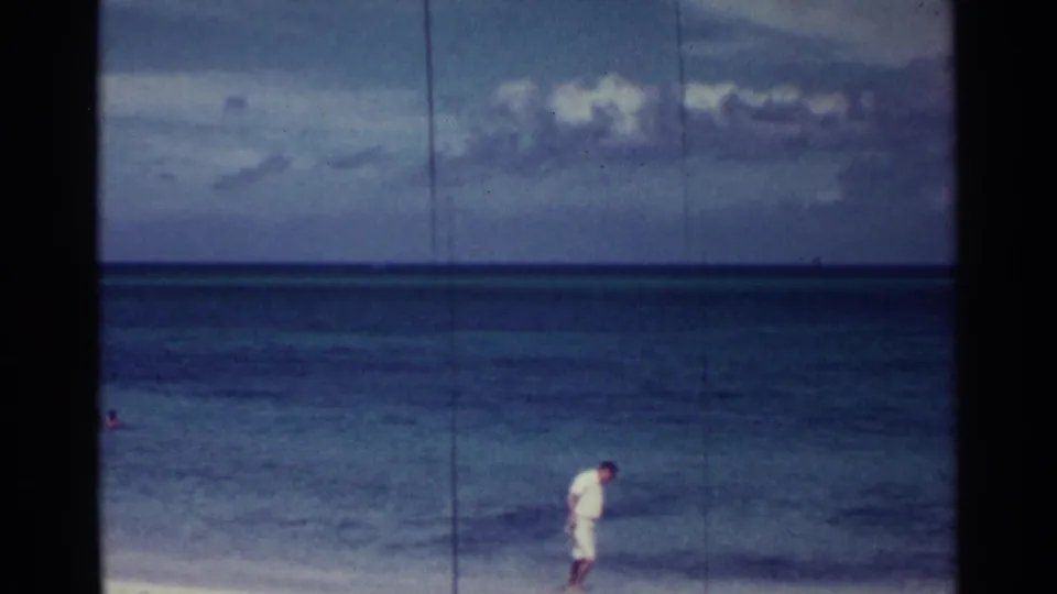 Soft 8mm view of the Nassau shoreline with a man near the beach edge and a swimmer partly visible in the water.