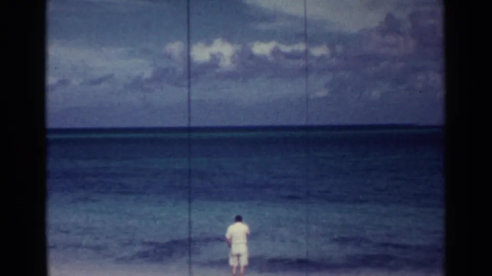 A man in light clothing stands near the Nassau shoreline facing the calm ocean in faded 1963 8mm footage.