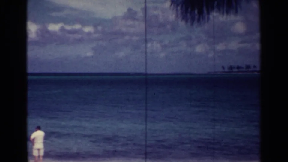 Nassau beach view from 1963 with a distant man facing the sea and palm silhouettes visible near the horizon.